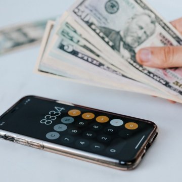 money in someones hand beside an iphone with a calculator app open